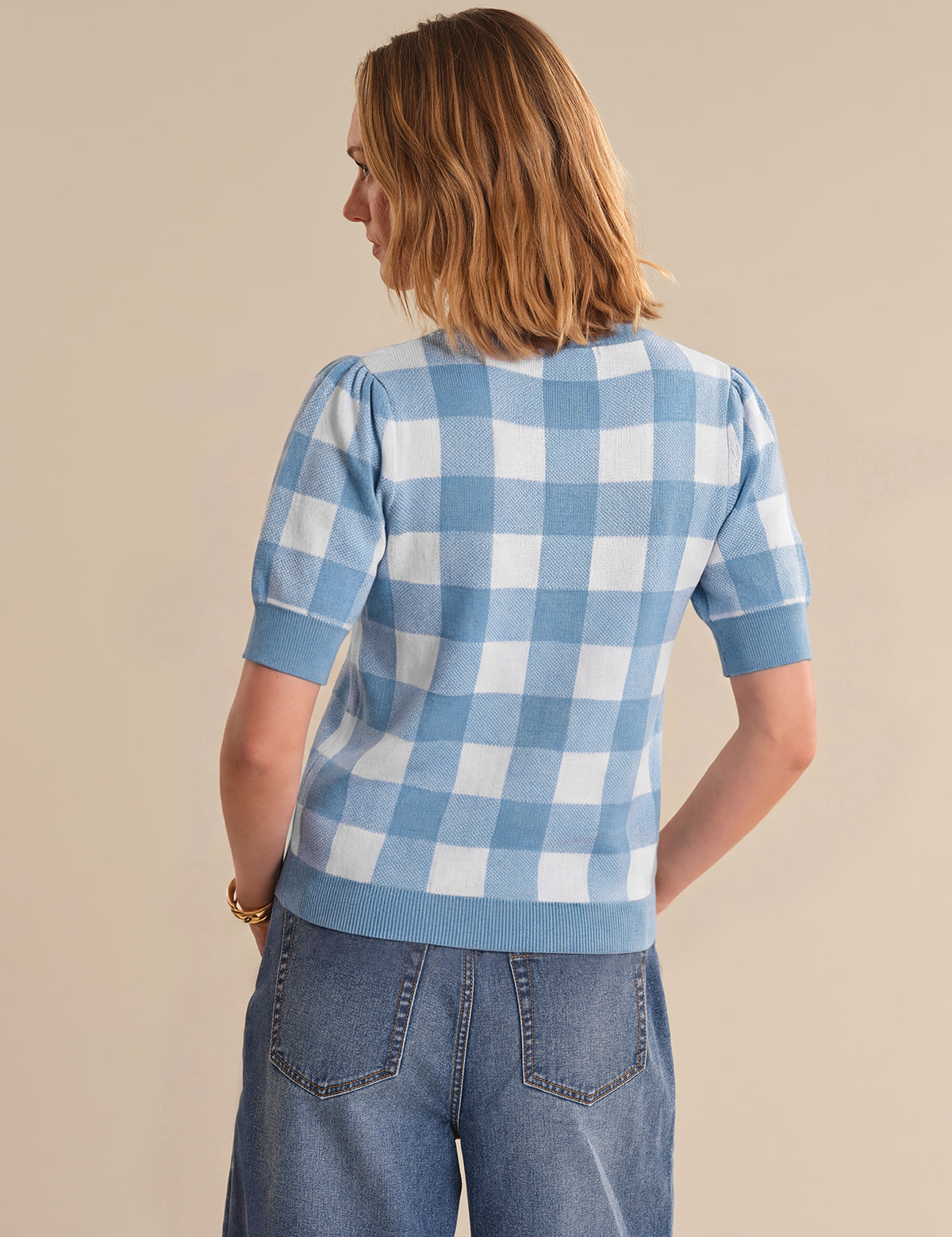 Person wearing a blue and white checkered shirt with short sleeves on a beige background