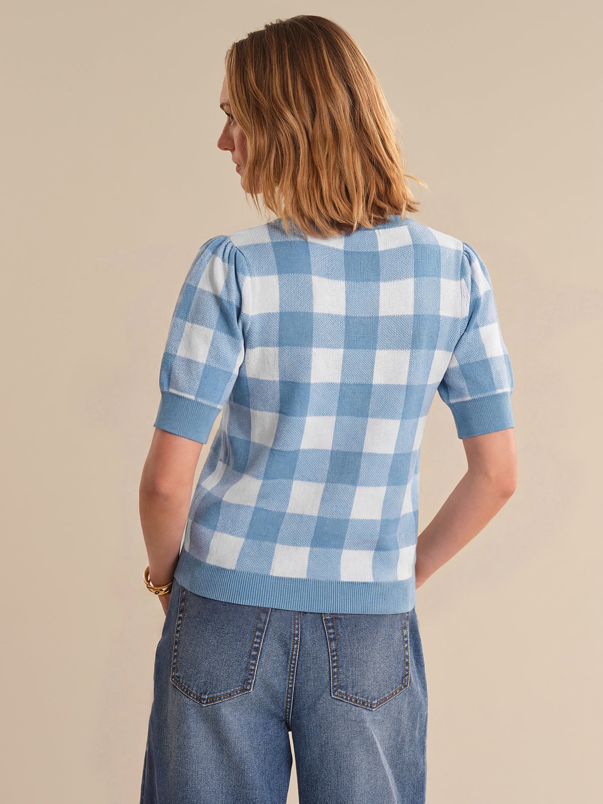 Person wearing a blue and white checkered shirt with short sleeves on a beige background