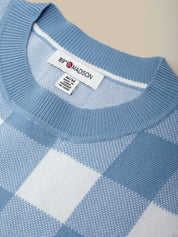 Close-up of a blue checkered sweater with a brand label on a beige background