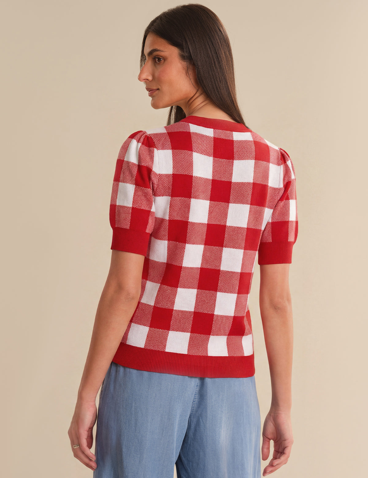 Woman wearing a red and white checkered top with puff sleeves on a beige background