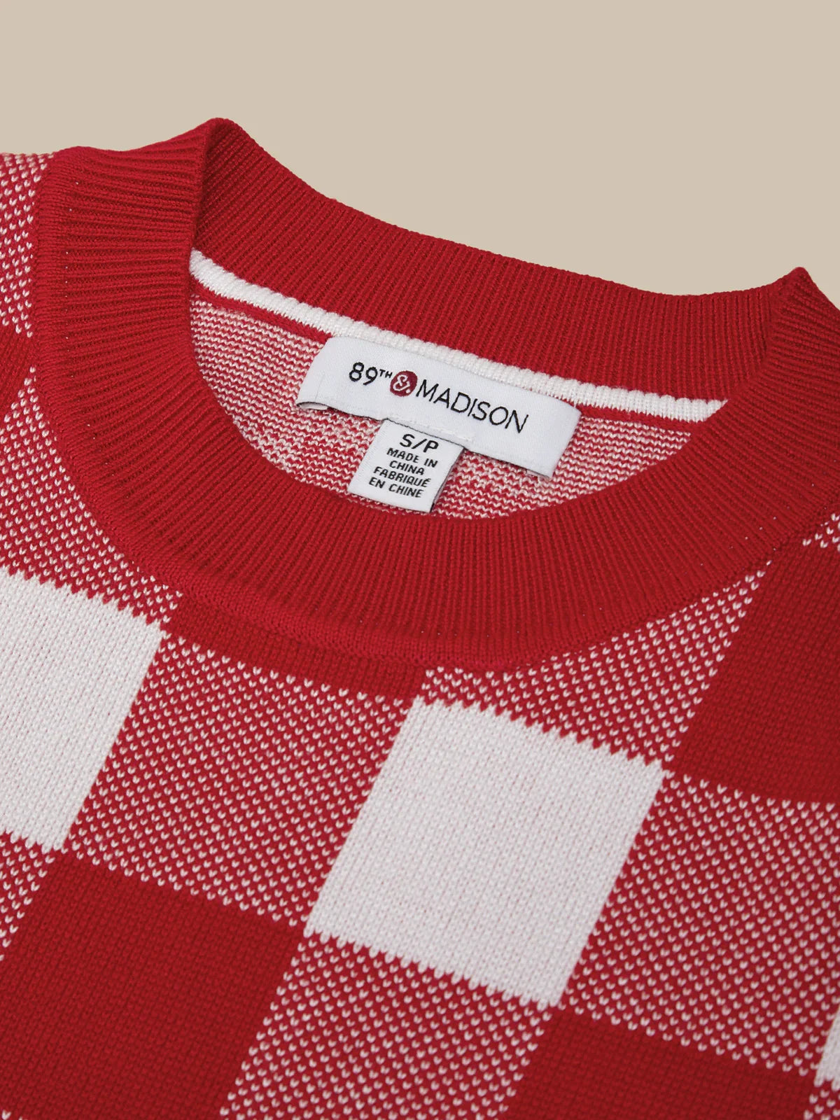 Red and white checkered sweater with '89th Madison' label on a beige background