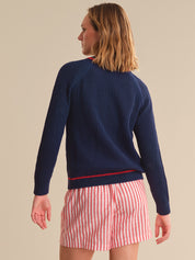 Woman wearing a navy blue knitted cardigan over a red and white striped shirt with beige shorts on a beige background.