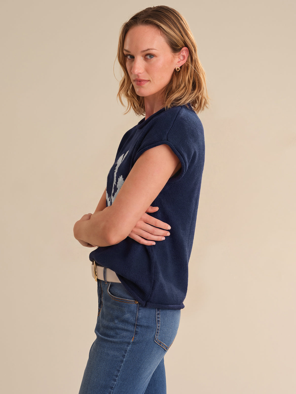Woman wearing a navy blue t-shirt and blue jeans against a beige background