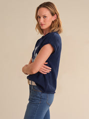 Woman wearing a navy blue t-shirt and blue jeans against a beige background