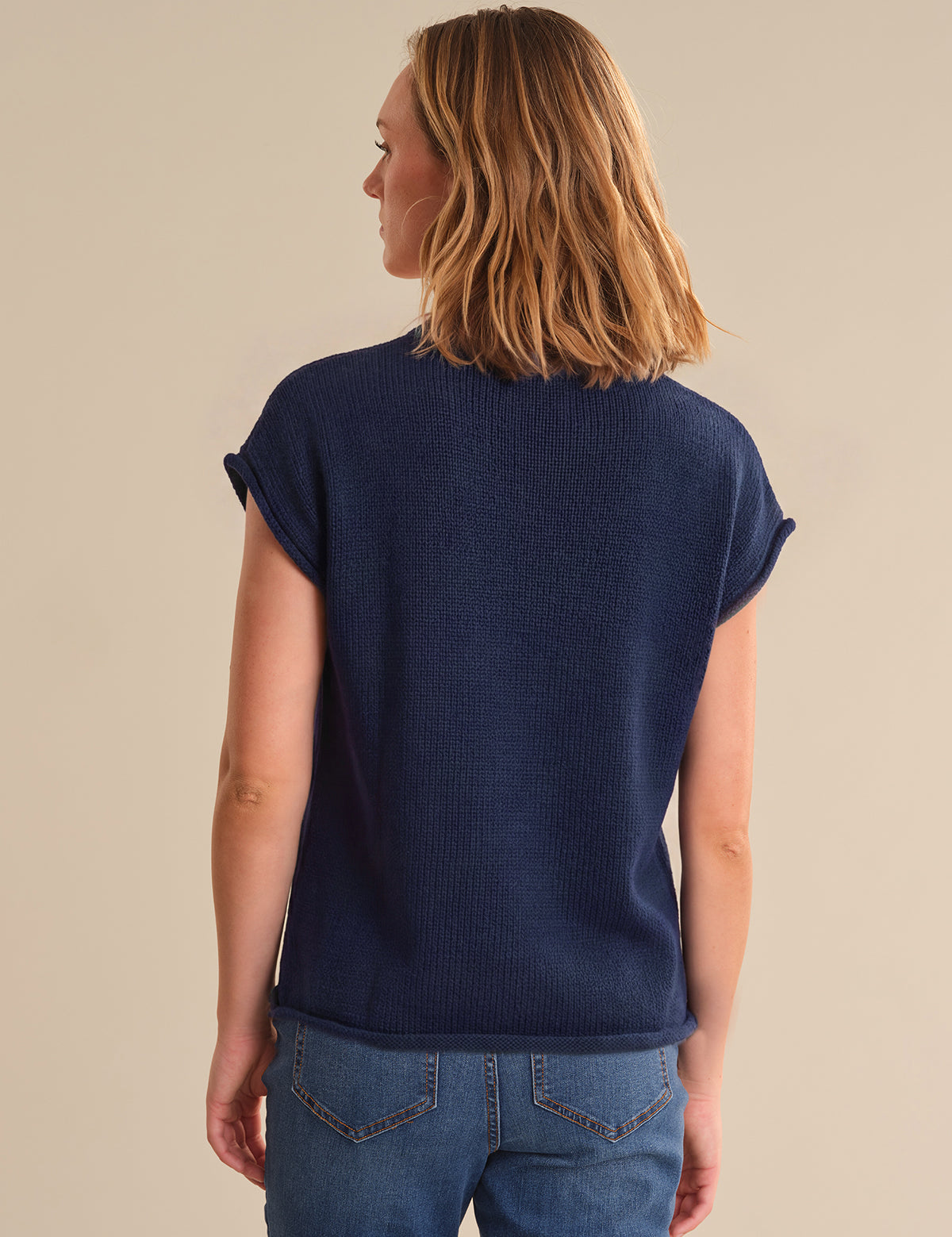 Person wearing a navy blue sweater and blue jeans on a beige background