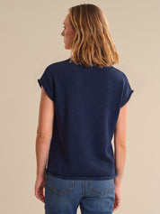 Person wearing a navy blue sweater and blue jeans on a beige background