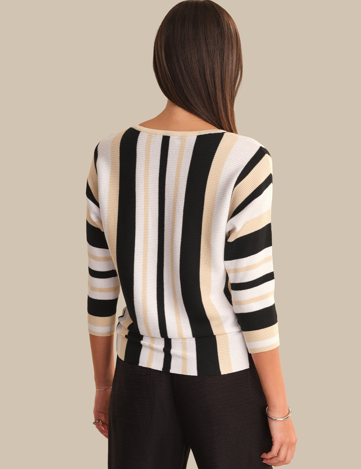 Woman wearing a black and beige striped sweater against a neutral background