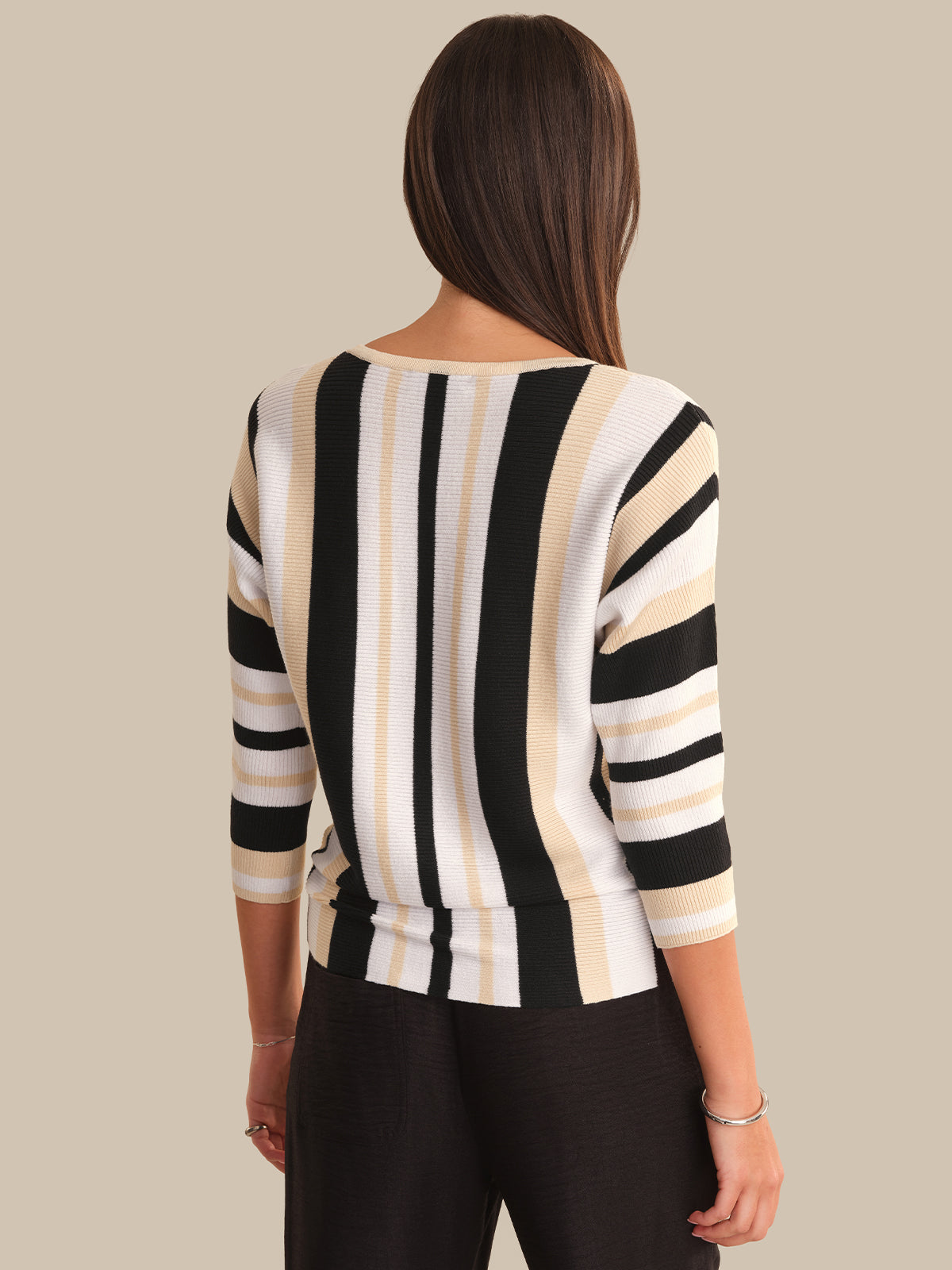 Woman wearing a black and beige striped sweater against a neutral background