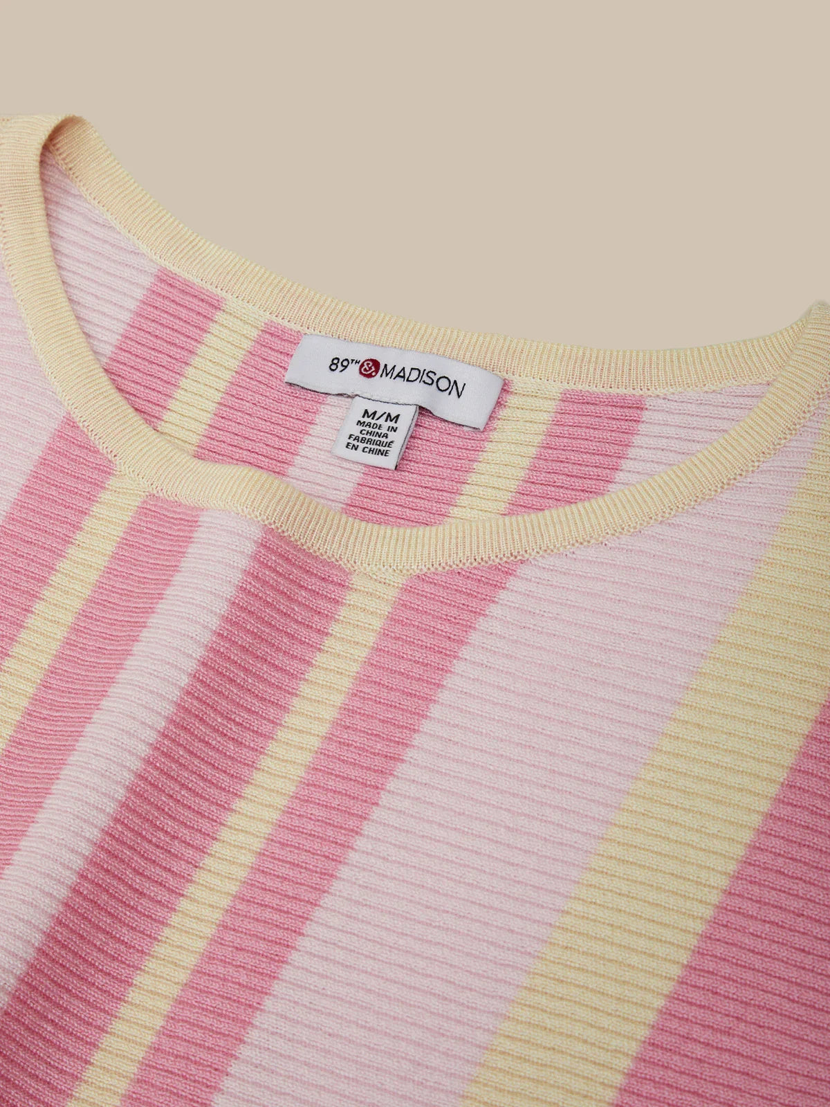 Close-up of a pink and yellow striped sweater with a brand label on a beige background