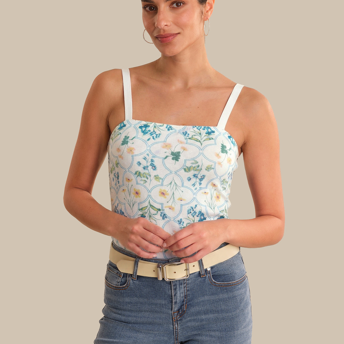 Woman wearing a floral tank top and jeans against a beige background