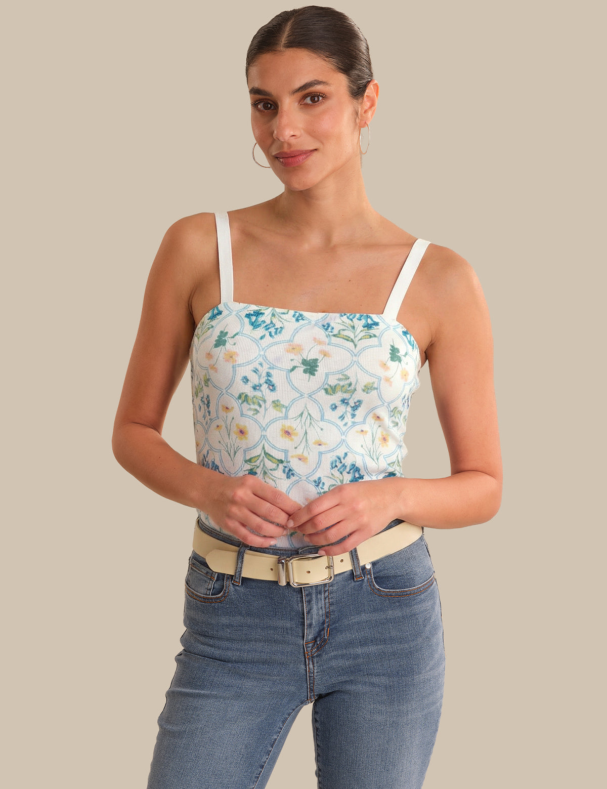 Woman wearing a floral tank top and jeans against a beige background