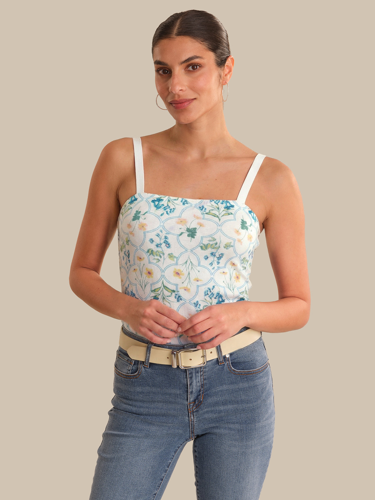 Woman wearing a floral tank top and jeans against a beige background