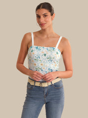 Woman wearing a floral tank top and jeans against a beige background