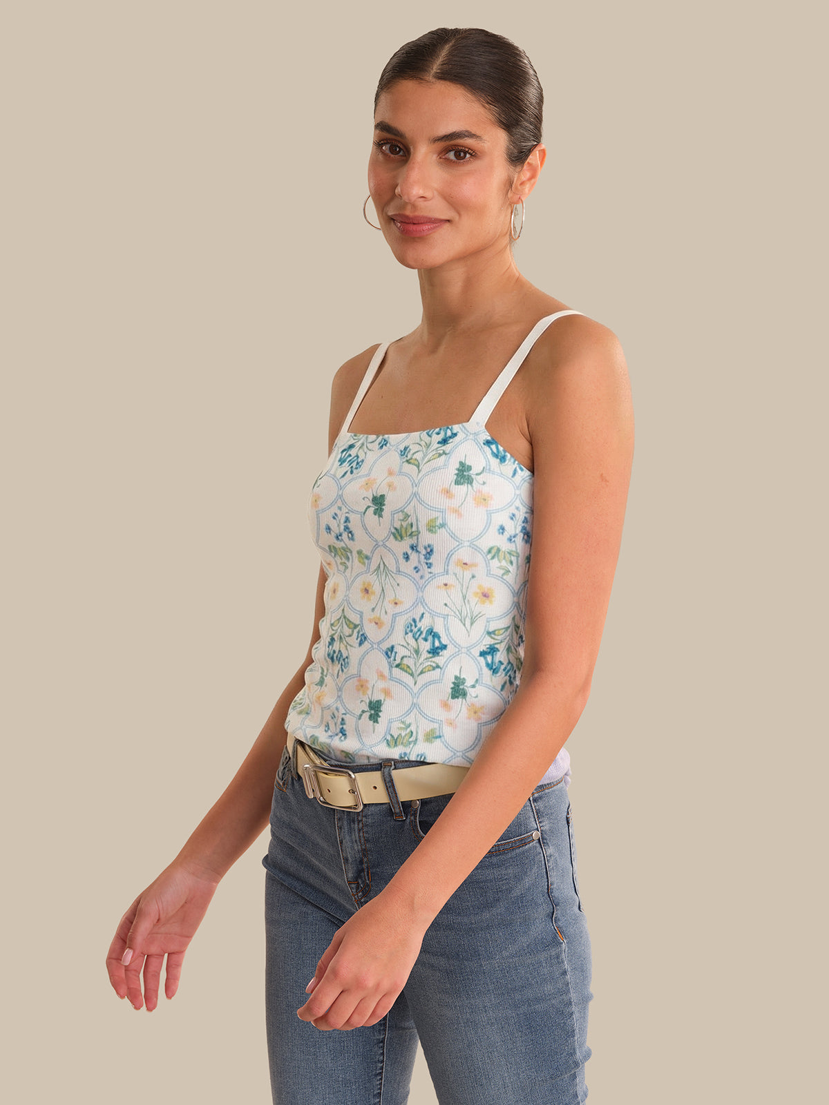 Woman wearing a floral camisole and jeans on a beige background