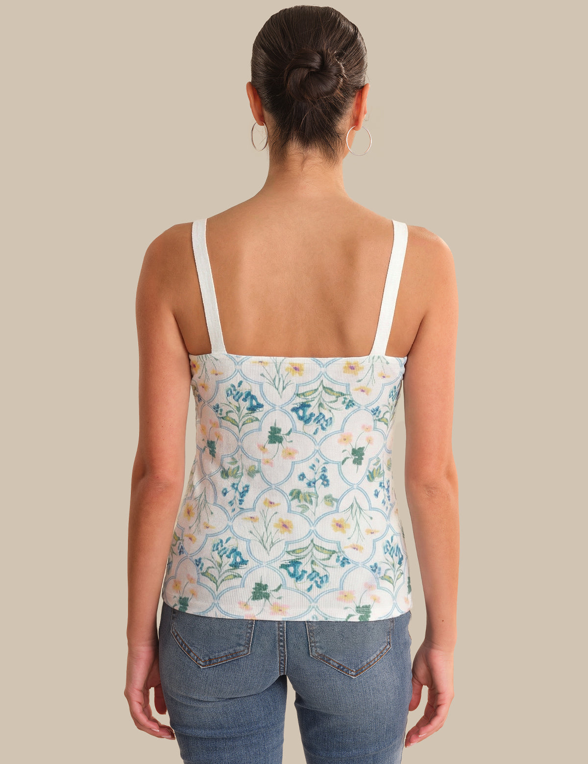 Woman wearing a floral tank top and jeans on a beige background