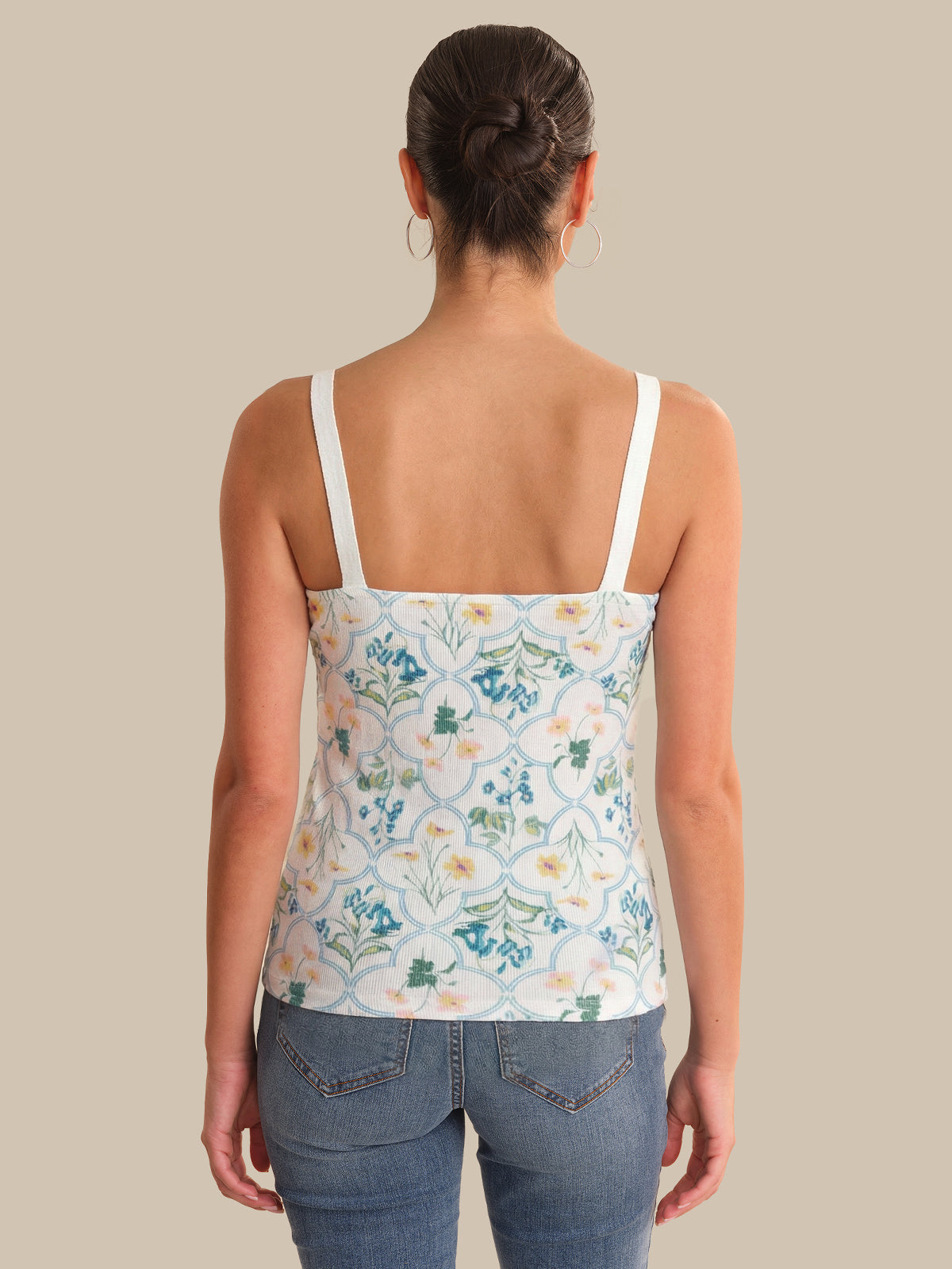 Woman wearing a floral tank top and jeans on a beige background