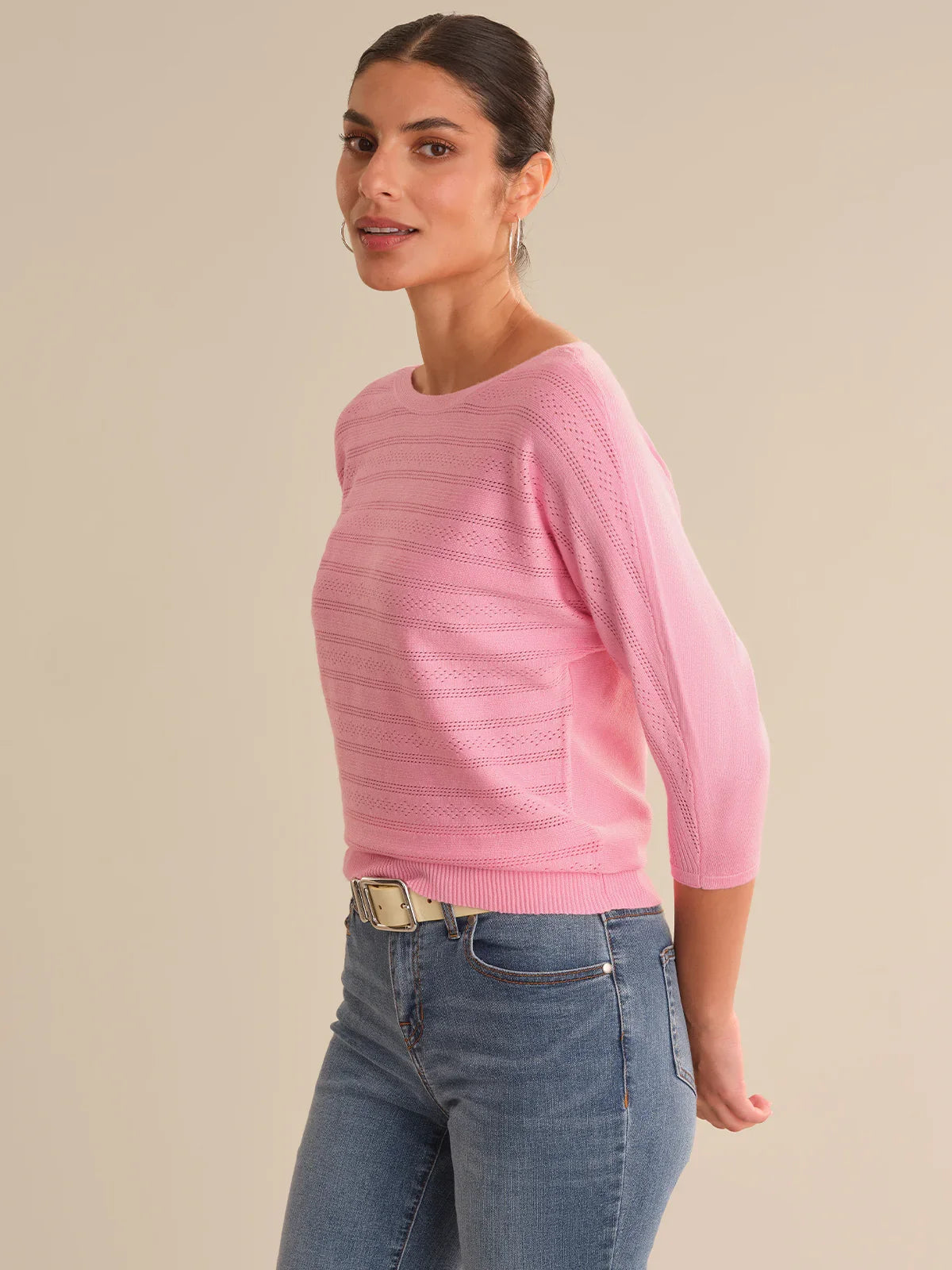 Woman wearing a pink sweater and blue jeans on a beige background