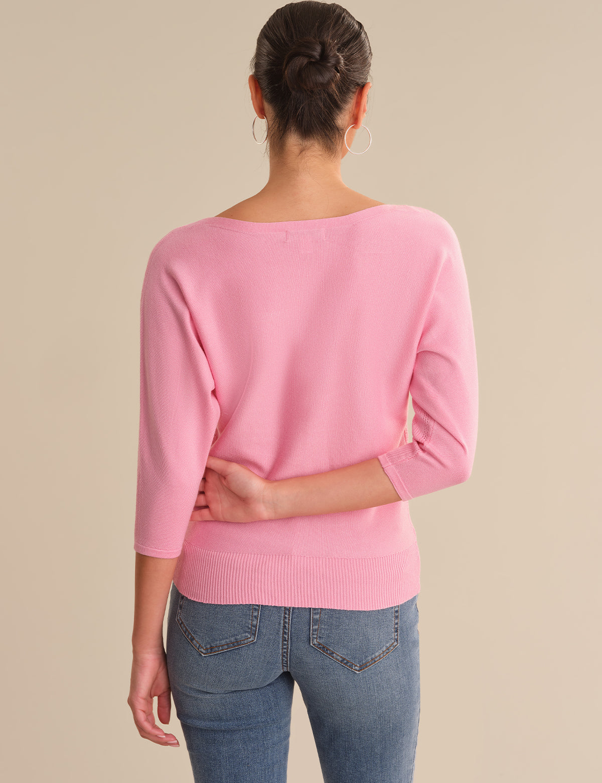 Person wearing a pink sweater and blue jeans on a beige background