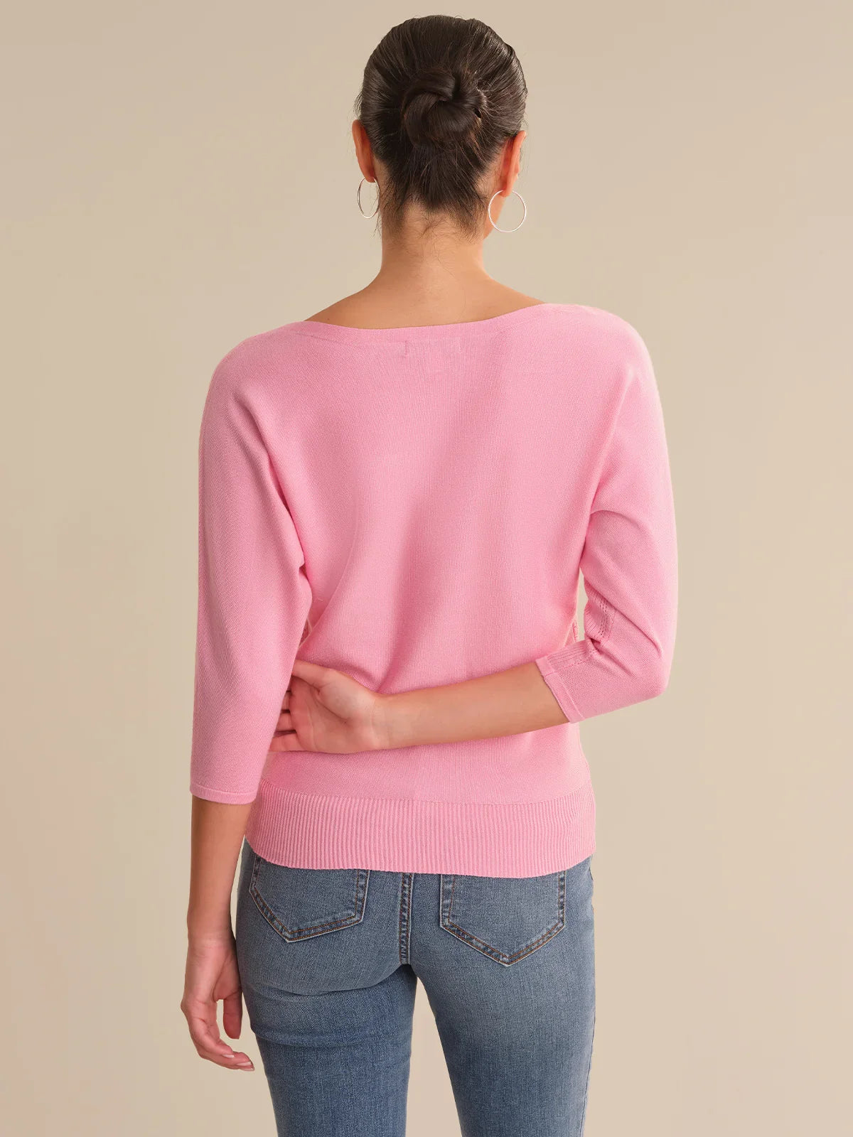 Person wearing a pink sweater and blue jeans on a beige background