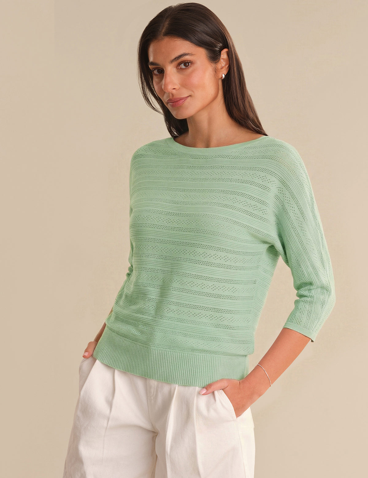 Woman wearing a light green sweater and white pants against a beige background