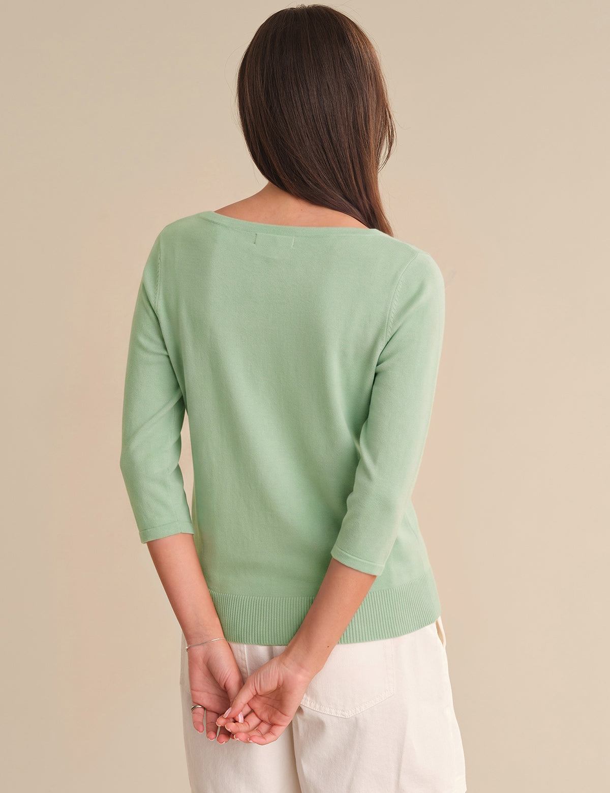 Person wearing a light green sweater and white pants on a beige background