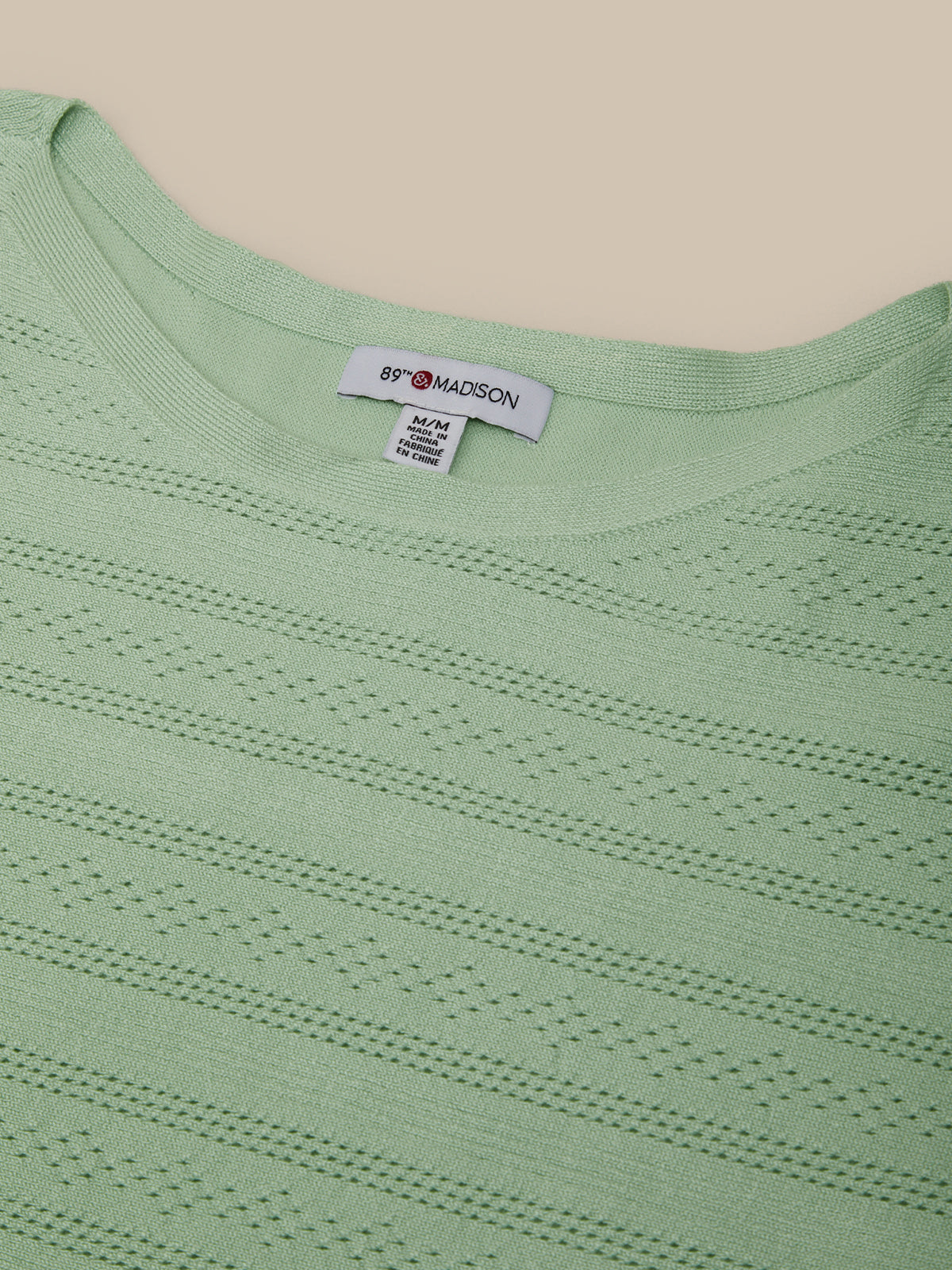 Close-up of a light green sweater with a brand label on a beige background