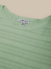 Close-up of a light green sweater with a brand label on a beige background