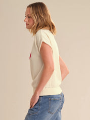 Woman wearing a light-colored sleeveless top and blue jeans against a plain background