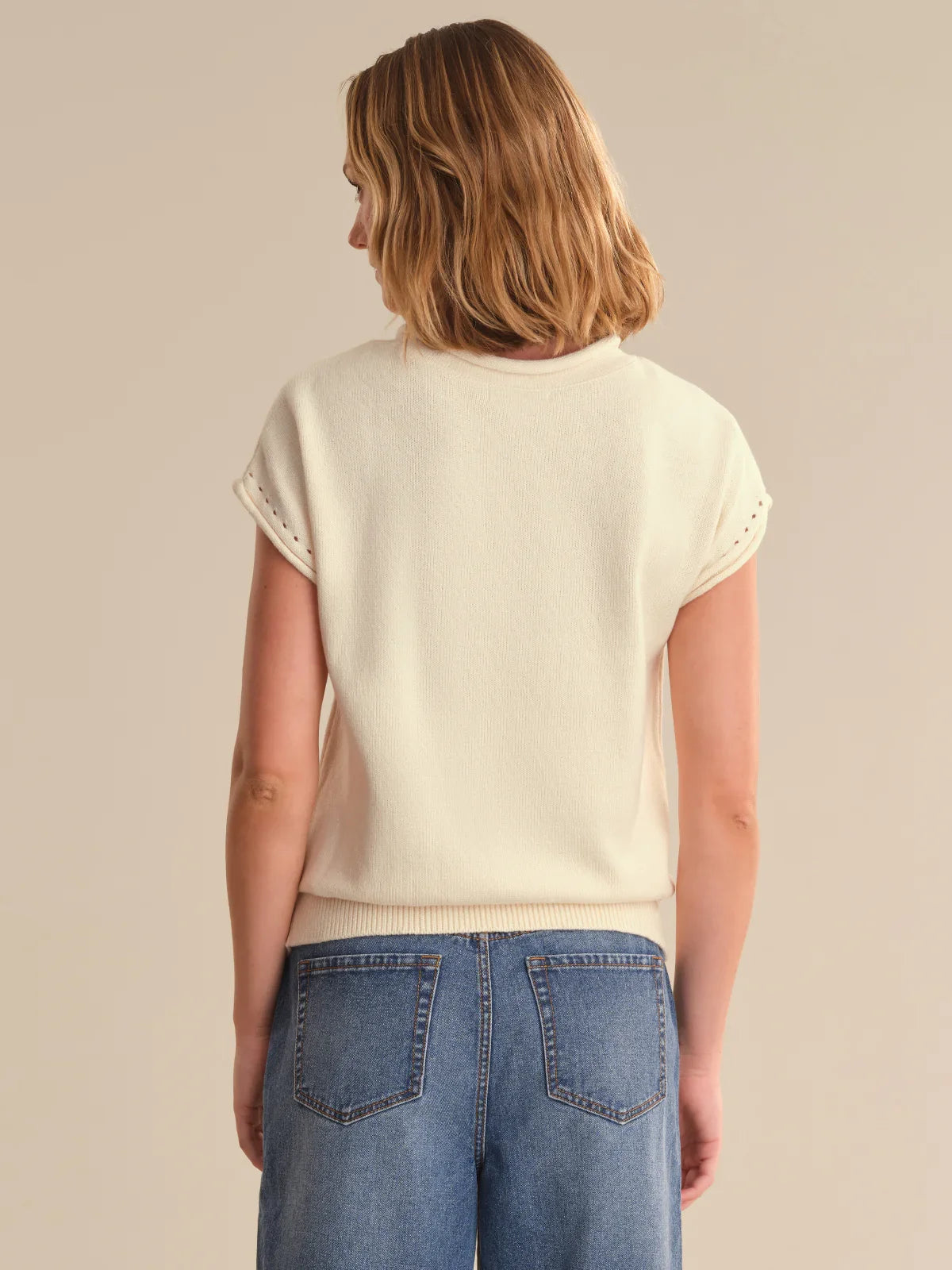 Woman wearing a cream sweater and blue jeans on a beige background