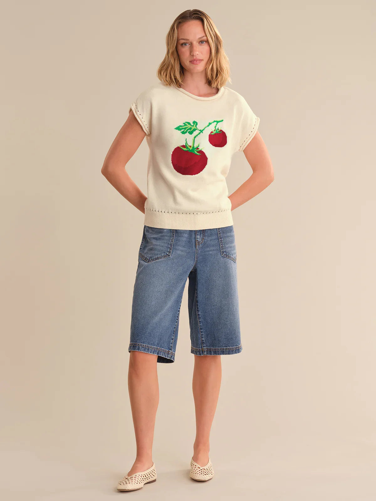 Woman wearing a white t-shirt with a cherry design and blue denim shorts on a beige background