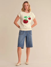 Woman wearing a white t-shirt with a cherry design and blue denim shorts on a beige background