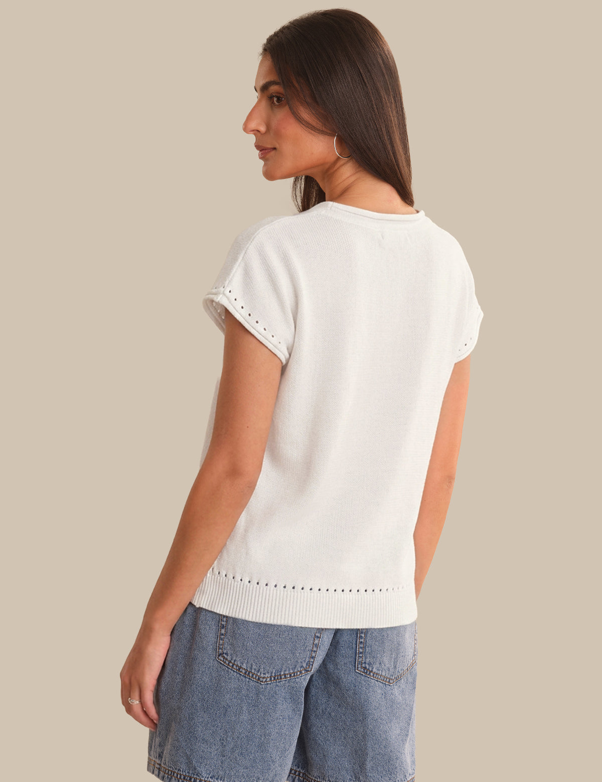 Woman wearing a white top with short sleeves and blue denim shorts on a beige background
