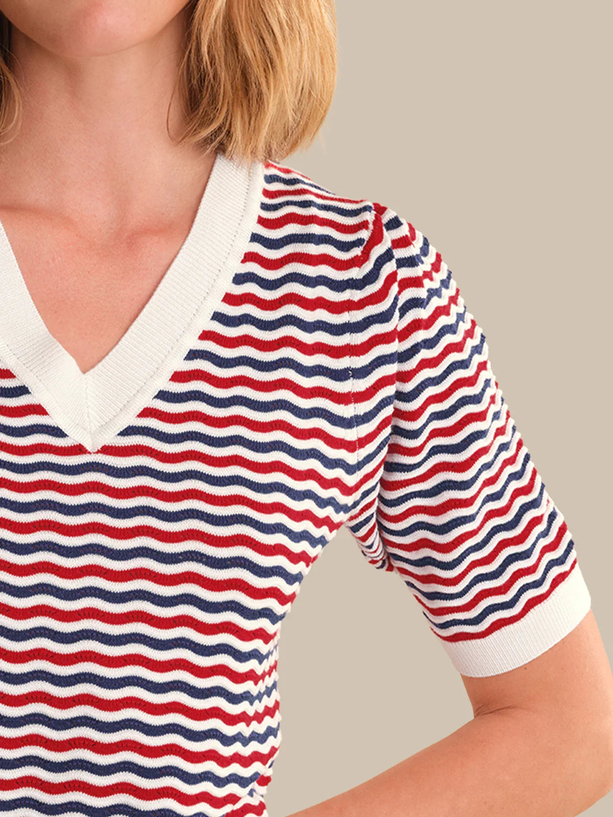 Person wearing a red, white, and blue striped shirt with a neutral background