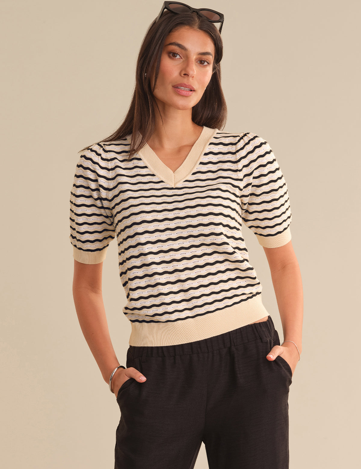 Woman wearing a black and white striped sweater with a beige collar against a beige background