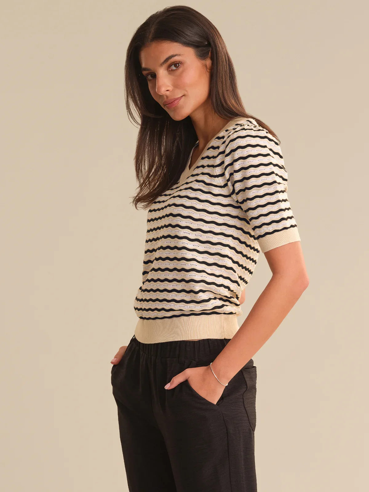 Woman wearing a black and white striped shirt with black pants on a beige background