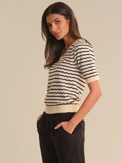Woman wearing a black and white striped shirt with black pants on a beige background