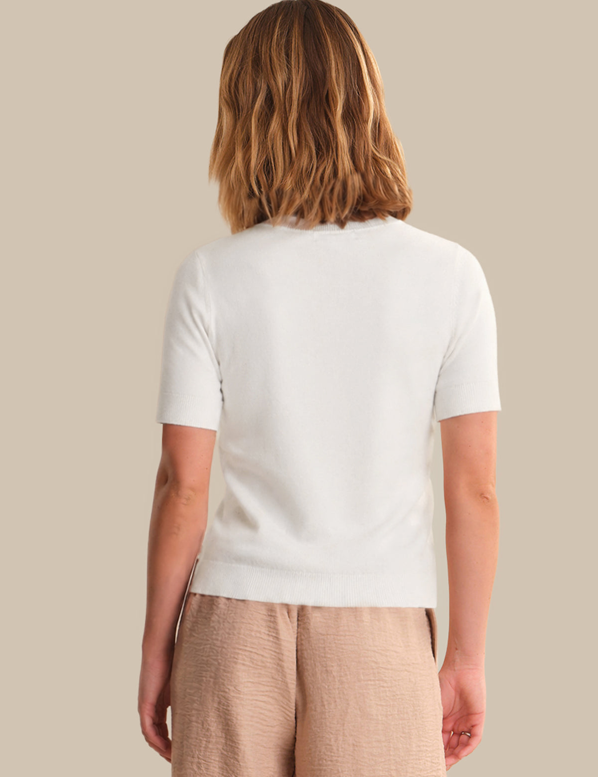 Person wearing a white t-shirt and beige pants on a beige background