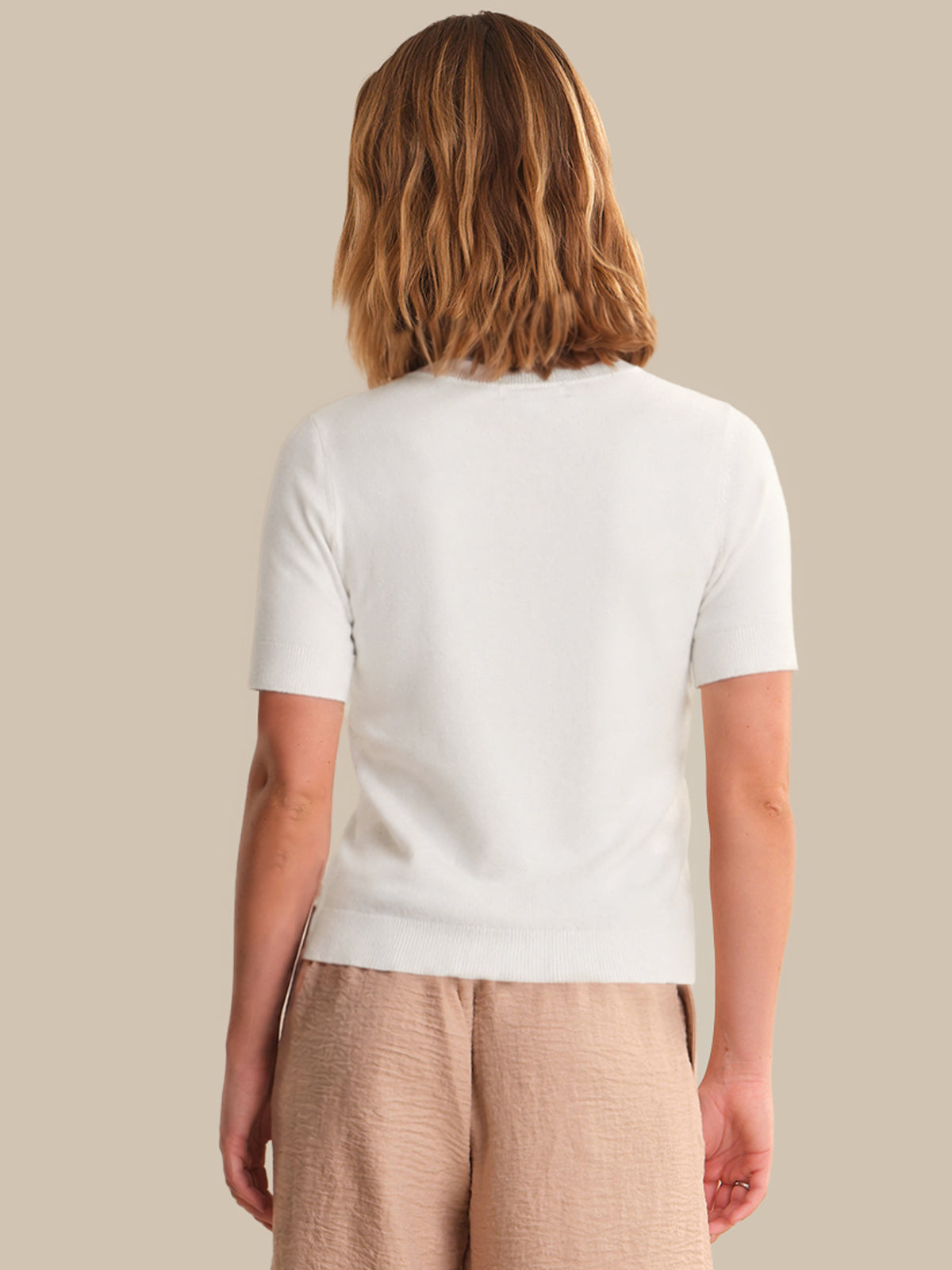 Person wearing a white t-shirt and beige pants on a beige background