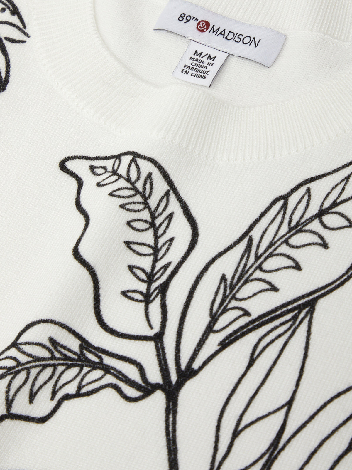 White sweater with black leaf pattern and '89 Madison' label.