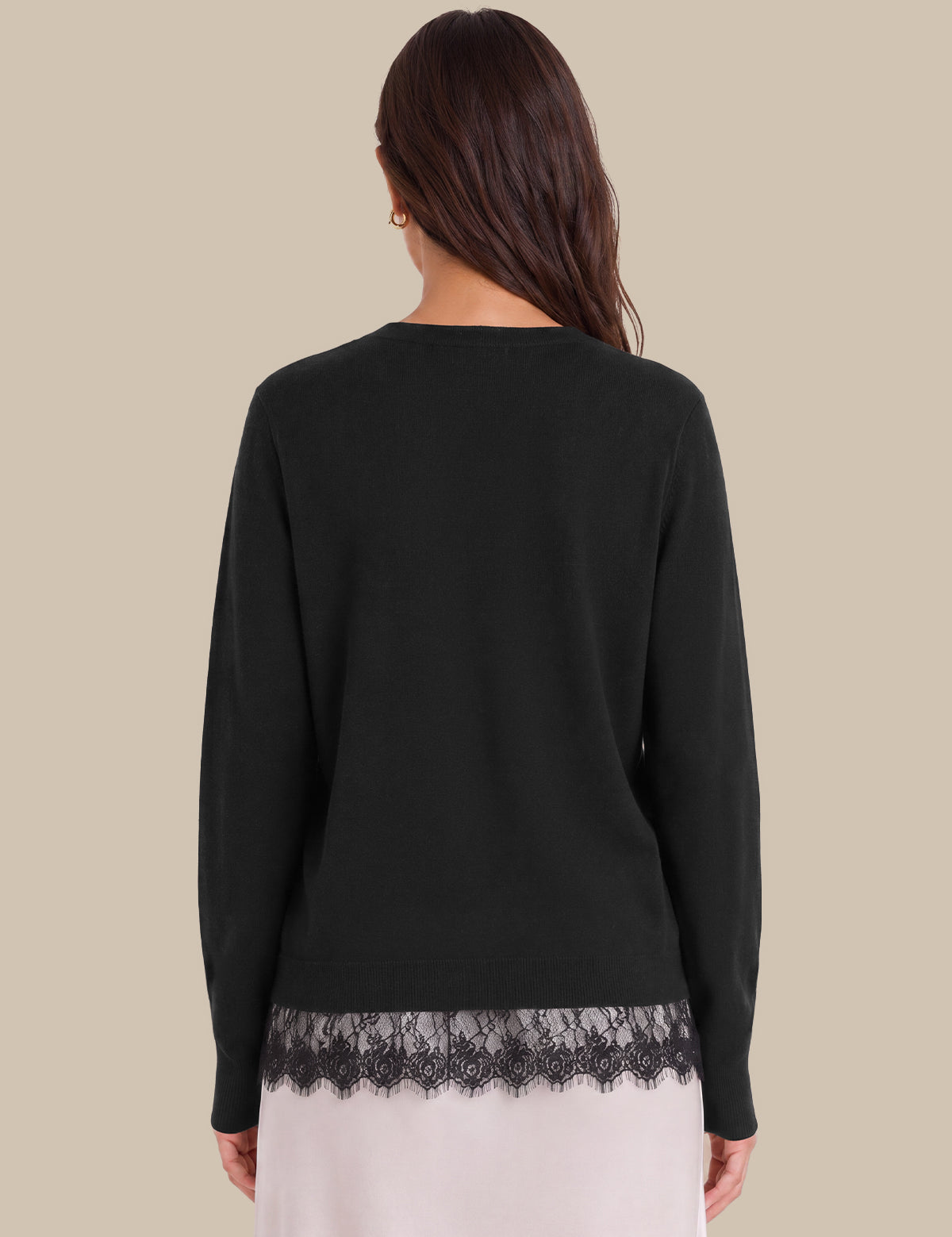 A woman shown from the back wearing a black long-sleeve top with a black lace hem, paired with a light pink skirt, against a solid beige background.