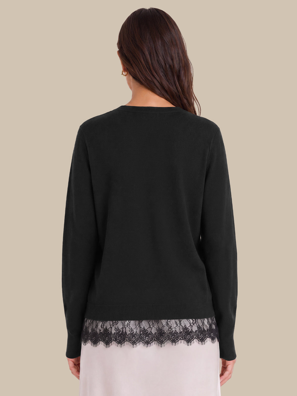 A woman shown from the back wearing a black long-sleeve top with a black lace hem, paired with a light pink skirt, against a solid beige background.