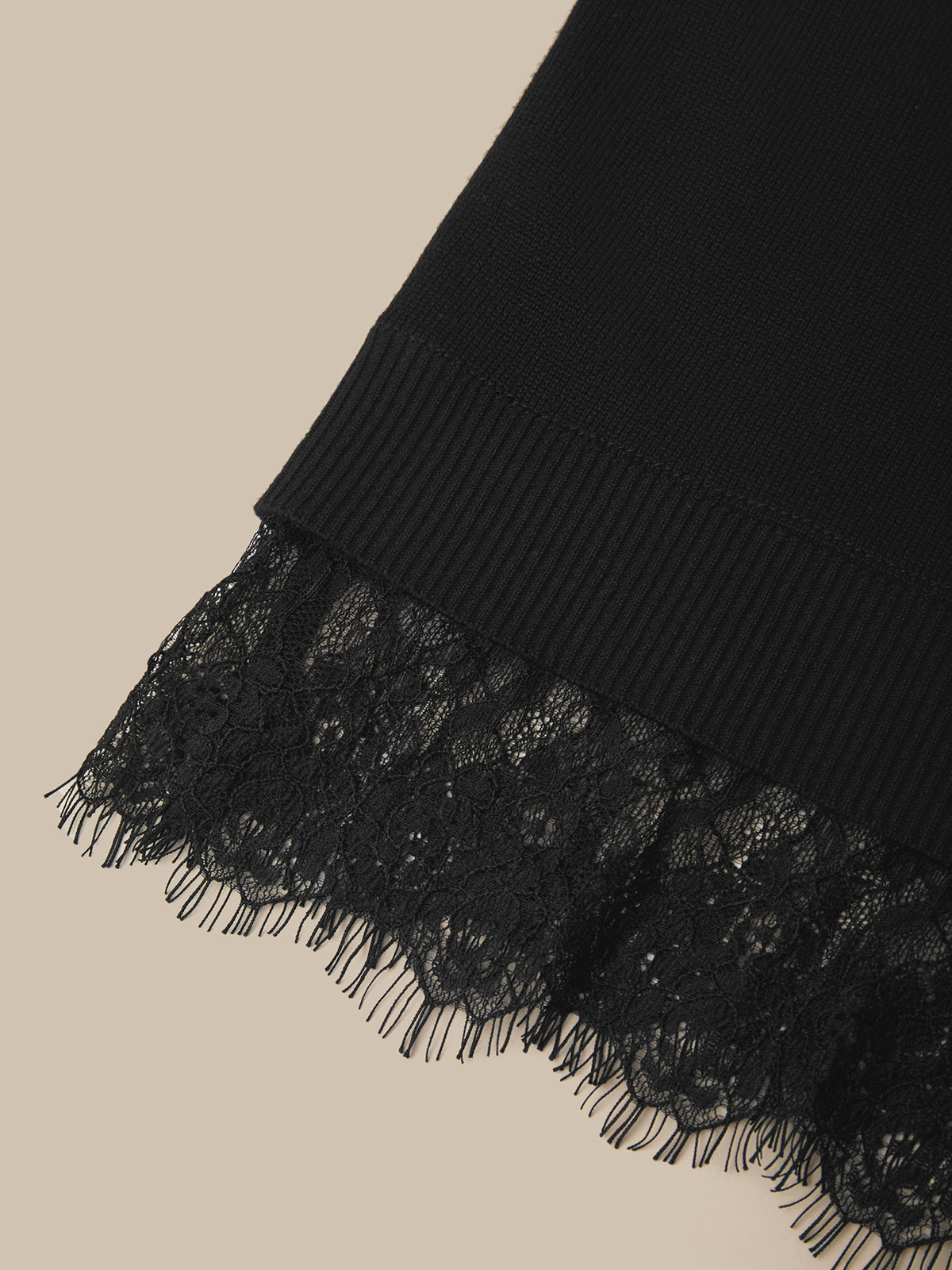 Close-up of a black ribbed knit fabric with a matching black lace ruffle trim, shown against a light beige background.