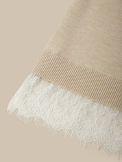 Close-up of a beige ribbed knit garment with a white floral lace hem, shown against a solid beige background.