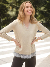 A woman wearing a beige knit sweater with a white lace V-neck trim and a matching lace hem, paired with black leggings, standing outdoors on a crosswalk.