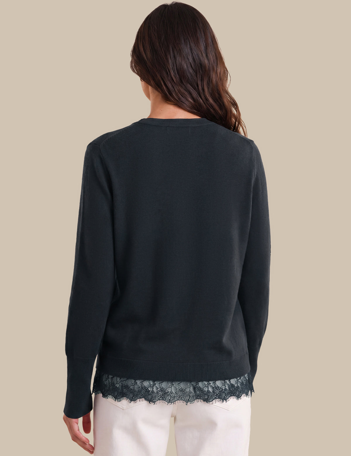 A woman shown from the back wearing a dark blue long-sleeve top with a lace hem detail, paired with white pants, against a solid beige background.