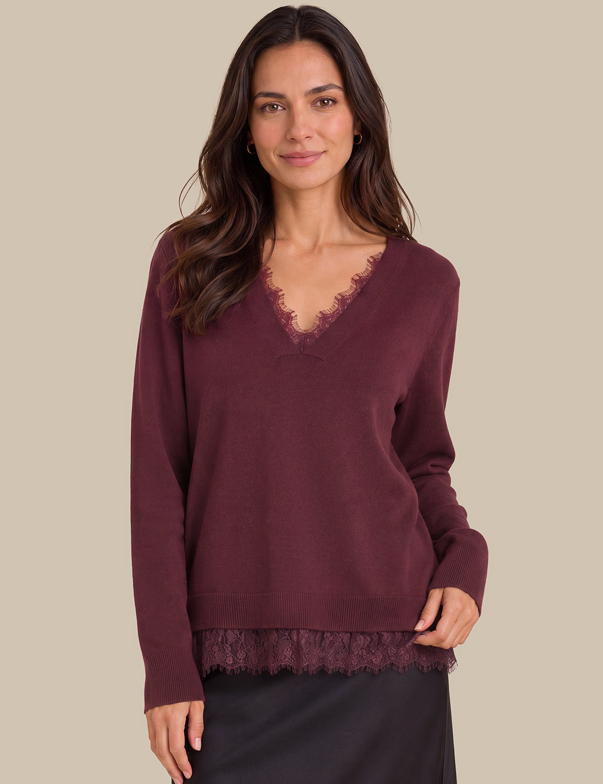 A woman wearing a long-sleeve burgundy knit sweater with a lace V-neck trim and matching lace hem, paired with a dark skirt, against a solid beige background.