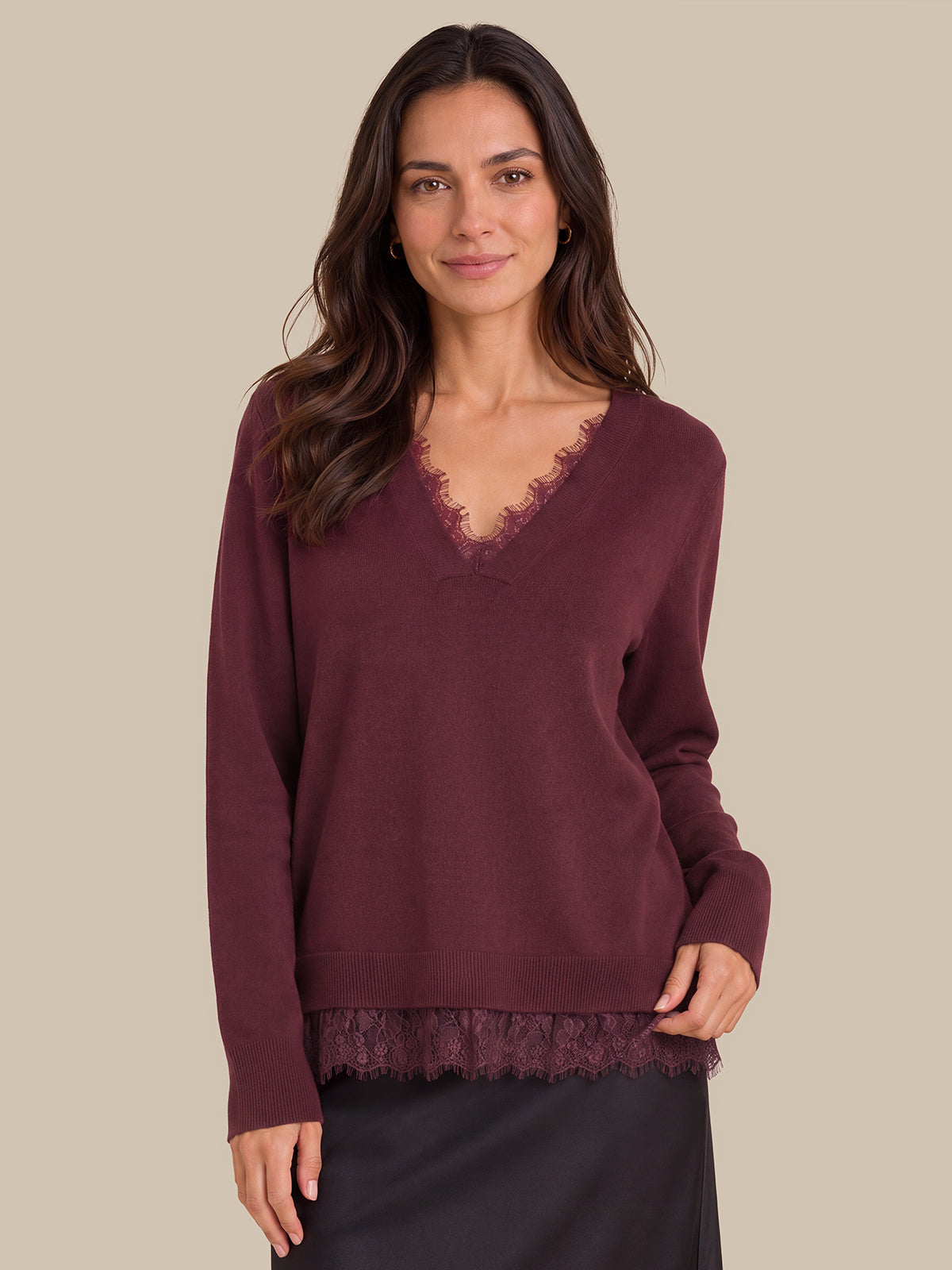A woman wearing a long-sleeve burgundy knit sweater with a lace V-neck trim and matching lace hem, paired with a dark skirt, against a solid beige background.