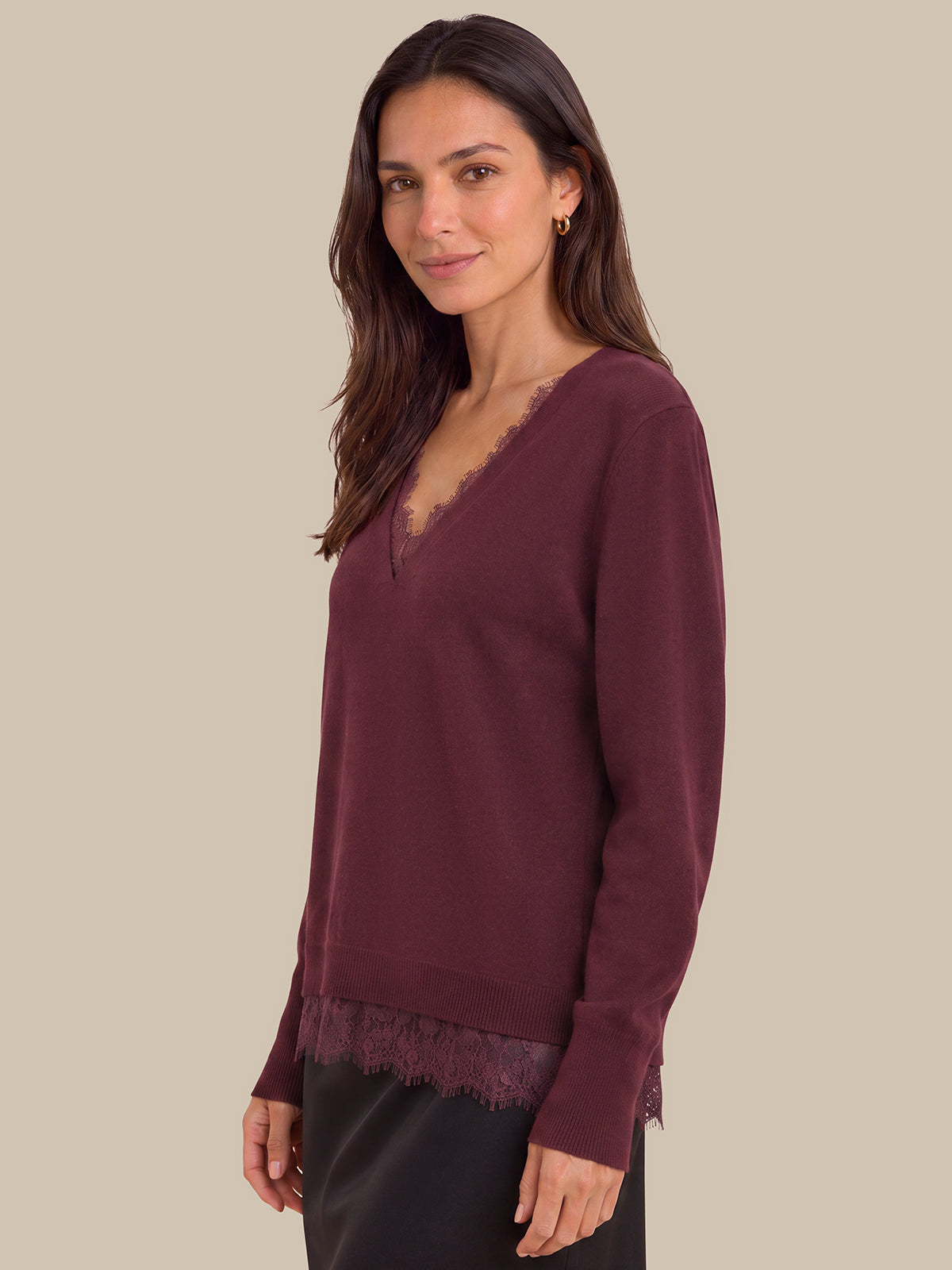 A woman wearing a long-sleeve burgundy knit sweater with a lace-trimmed V-neck and hem, paired with black bottoms, against a solid beige background.