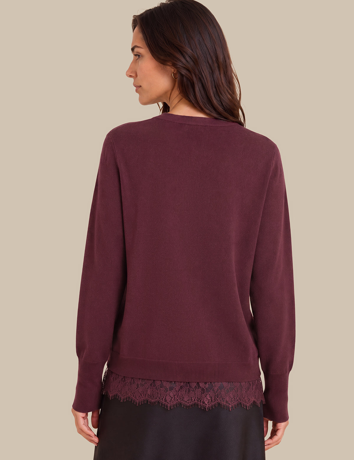 A woman shown from the back wearing a long-sleeve crewneck sweater in a deep burgundy or plum color, featuring a lace hem detail, against a solid beige background.