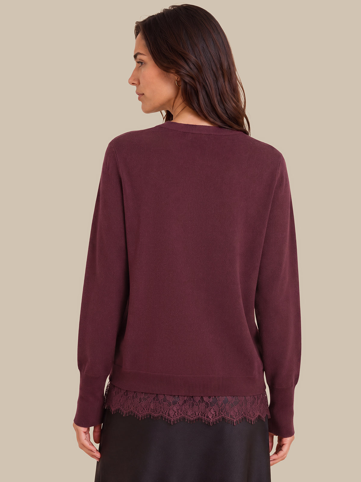 A woman shown from the back wearing a long-sleeve crewneck sweater in a deep burgundy or plum color, featuring a lace hem detail, against a solid beige background.